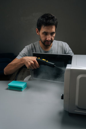 Vertical portrait of housekeeper cleaning and sanitizing microwave oven with steam cleaner device, eliminating germs and tough stains, maintaining hygiene in kitchen at home.の写真素材
