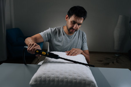 Cleaning service employee performing household chore, steam cleaning and sanitizing pillow, ensuring hygiene, purity and disinfection in bedroom, promoting health and wellness through deep cleaning.の写真素材