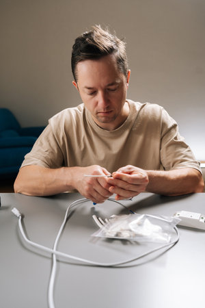 Vertical portrait of man working with electronic components, stripping insulation from cable repairing, assembling wiring, demonstrating hobby electronics project or household electrical maintenance.の写真素材