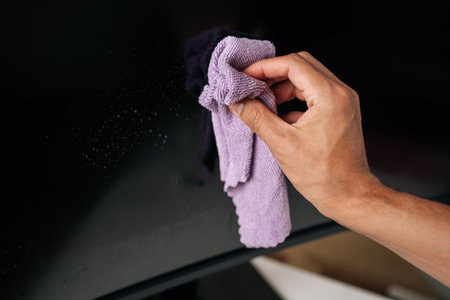 Close-up of man cleaning large curved computer monitor screen with microfiber cloth, ensuring spotless and clear display for optimal viewing. Concept of hygiene and cleanliness in domestic environmentの写真素材