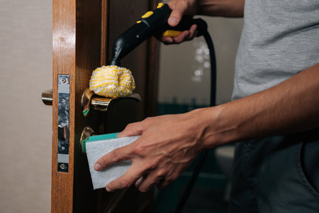 Close-up of man steam cleaning door handle for deep disinfection, killing germs and sanitizing frequently touched surfaces in home, ensuring hygiene and healthy environment.の写真素材