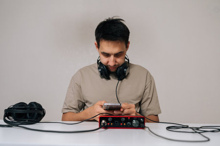 Man creating or enjoying music on smartphone connected to audio interface, wearing headphones, demonstrating modern portable sound production or listening experience.の写真素材