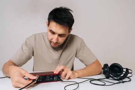 Portrait of audio engineer male holding red usb audio interface card and plugging cable into headphone output, setting up for music creation, sound recording, and mixing in home studio.の写真素材
