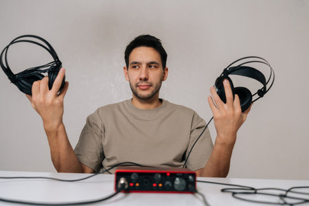 Portrait of audio engineer experiencing dilemma choosing between different studio headphones, comparing sound quality during music production, audio recording, mixing, podcasting with audio interface.の写真素材