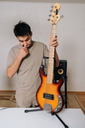 Vertical portrait of male musician, standing alongside bass guitar on stand, deeply concentrating...