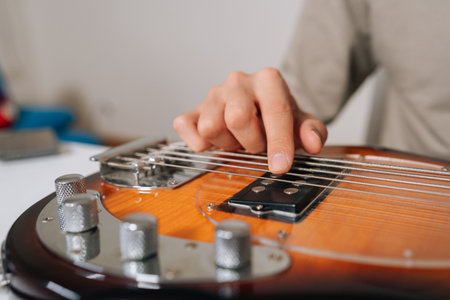 Close-up of musician hand plucking and adjusting bass guitar strings, preparing and tuning instrument for practice, rehearsal or live performance with focused precision.の写真素材