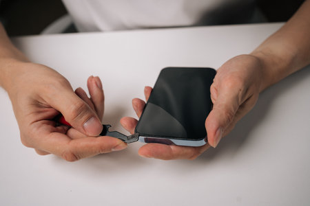 Close-up of technician removing broken tempered glass screen protector from smartphone using...