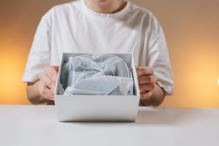 Cropped shot of female hands opening white box to reveal new wireless gamepad wrapped in tissue...