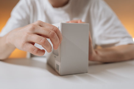 Hands opening white electronics box to reveal new wireless console game controller, close-up...