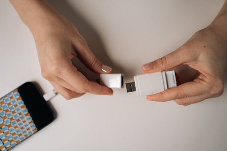 Top view of young adult woman hands connecting USB flash drive to smartphone using adapter cable...