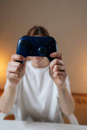 Vertical shot of female gamer playing video games with dark blue wireless controller, holding up,...