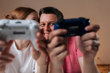 Cheerful young couple enjoying home entertainment, holding wireless video game controllers, bonding...