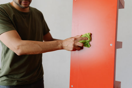 Cropped shot of man cleaning red shelf with rag, ensuring dust-free and spotless surface for books and decorative items, enhancing organization and hygiene at home. Concept of household cleanliness.の写真素材