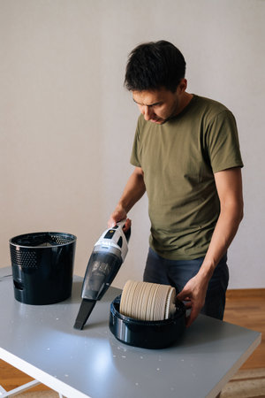 Vertical portrait of man cleaning table with air humidifier using small vacuum cleaner,...