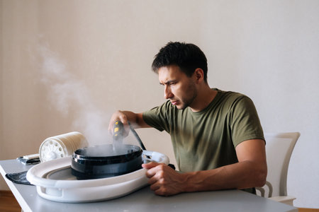 Focused housekeeper male cleaning filter of air humidifier with steam cleaner, promoting optimal performance and maintaining high standards of hygiene for indoor air quality.の写真素材