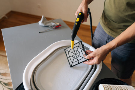 Close-up of cleaning service employee using steam cleaner to clean air humidifier filter in basin at...