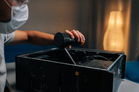 Closeup of technician in face mask and safety glasses cleaning computer case using small vacuum cleaner, demonstrating proper maintenance procedures. Concept of service, repair and cleaning computerの写真素材