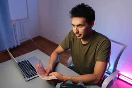 Top view of cashier counting banknotes sitting working at desk with laptop and money counter machine, illustrating financial accounting in modern office environment.の写真素材