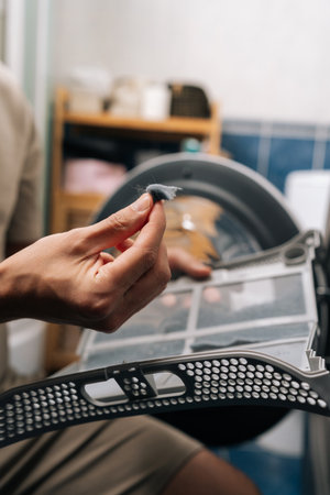 Male hand removing accumulated lint and fibers from tumble dryer filter, highlighting importance of regular cleaning for appliance maintenance and efficient operation.の写真素材