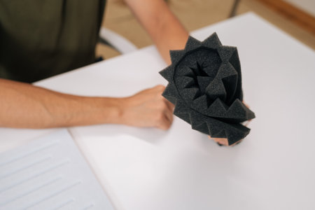 Close-up of male hand holding soundproof foam panel, checking acoustic material before installation. Concept of sound insulation, noise reduction and studio treatment materials.の写真素材