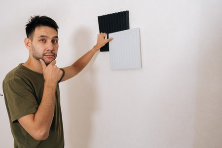 Portrait of thoughtful handyman choosing between two types of soundproof wall panels, comparing designs and textures while installing for acoustic treatment in room, enhancing sound quality.の写真素材