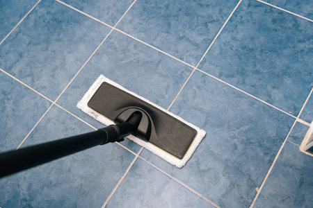 High-angle view of steam cleaner sanitizing blue tiled bathroom floor, releasing steam for deep...