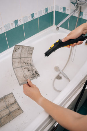 Vertical cropped shot of professional HVAC technician using vacuum cleaner to remove dust and dirt from dirty air conditioner filter in bathroom, performing maintenance and improving air quality.の写真素材