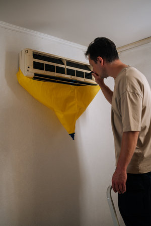 Vertical shot of focused HVAC technician using flashlight, inspecting air conditioning unit covered with yellow drop cloth during maintenance or repair service. Concept of air condition maintenanceの写真素材