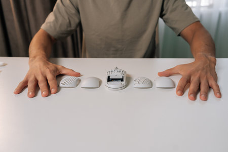 Person hands on white desk showing disassembled ergonomic wireless computer mouse with core unit and...