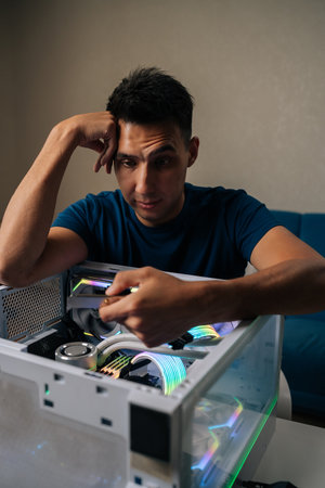 Vertical portrait of puzzled technician upgrading desktop computer by installing wi-fi module, focusing intently on task with thoughtful expression, showcasing expertise and attention to detailの写真素材
