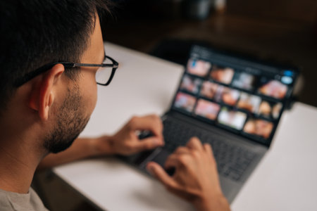 Back view of man in eyeglasses navigating laptop touchpad during video conference, highlighting remote working technology and digital connectivity. Concept of remote working on distance workplace.の写真素材