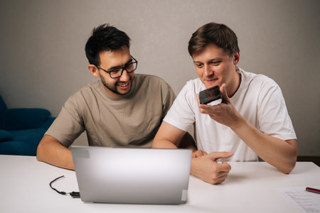 Portrait of two young start-up men in office collaborating on startup plan, using smartphone for...