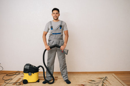 Full length portrait of professional cleaning service worker in coverall holding washing vacuum cleaner, getting ready to cleaning in living room standing posing on white background, looking at cameraの写真素材