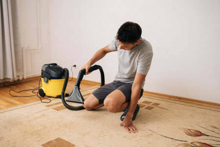 Housekeeper male using professional washing vacuum cleaner to remove dirt and dust from carpet, ensuring clean and healthy home environment. Concept of household chores and hygiene.の写真素材