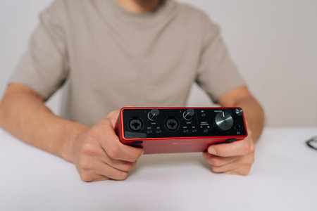 Close-up hands of sound engineer or musician holding compact red audio interface, crucial piece of...