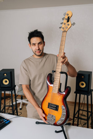 Vertical portrait of bearded musician posing in home studio, holding electric bass guitar and...
