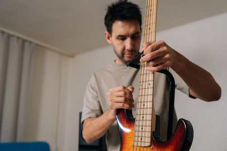 Portrait of focused musician male preparing for practice, carefully adjusting bass guitar on stand...