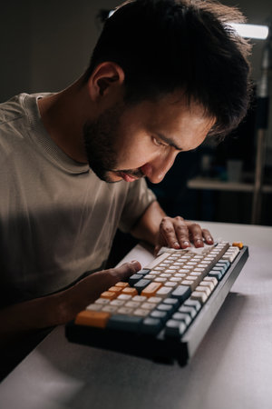 Vertical shot of young man examining and cleaning custom mechanical keyboard, ensuring detailed...