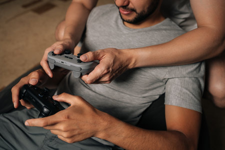 Closeup cropped shot of gay male couple relaxing at home, having fun playing video games together,...