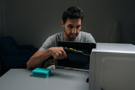 Man cleaning microwave interior with handheld steam cleaner, blasting hot vapor to lift grease and...