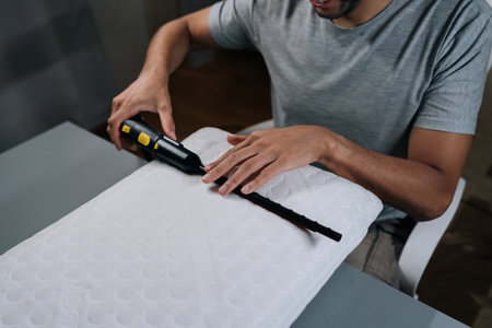 Man performing household chore, steam cleaning and sanitizing pillow, ensuring hygiene, purity and...