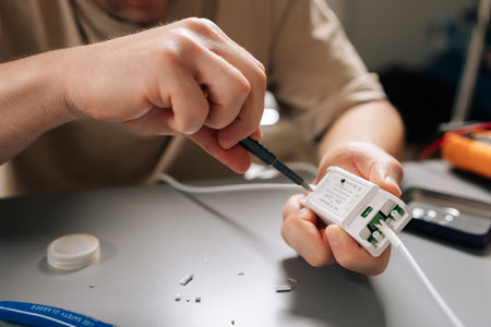 Close-up hands of unrecognizable technician repairing damaged electrical cable using screwdriver,...
