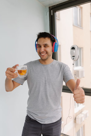 Vertical portrait of happy man in headphones giving thumbs up smiling looking at camera enjoying tea...