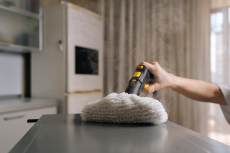 Hand using steam cleaner with fluffy white pad, removing dirt and germs from kitchen appliance surface, emphasizing eco-friendly and chemical-free cleaning concepts.の写真素材
