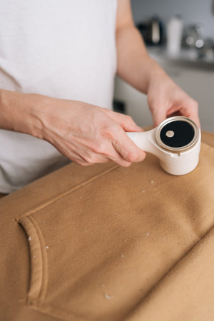 Vertical cropped shot of person using electric fabric shaver, removing pilling and fuzz from sweatshirt, maintaining clothing appearance and textile quality through effective garment care, close-up.の写真素材