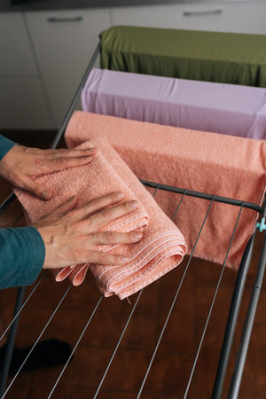 Hands arranging clean peach towels, along with other colorful textiles, on metal drying rack...