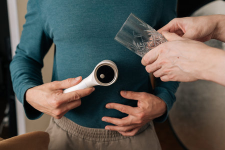 Person holding electric lint remover, operating garment care device on teal sweater to smooth fabric surface and remove pilling, improving textile look.の写真素材