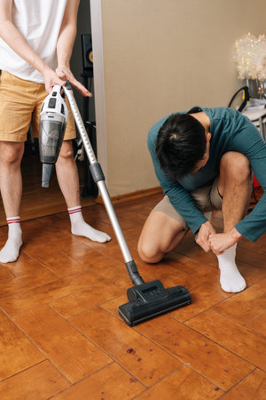 Vertical shot of two men performing household maintenance together, with one using vacuum to tidy up...