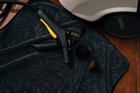 Steam cleaner nozzle, hose and interchangeable brush attachments resting on dark gray microfiber cloth, ready for thorough household sanitizing. Concept of household chores, cleanliness.の写真素材
