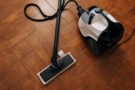Steam cleaner appliance and flat mop attachment resting on warm brown herringbone tile floor, signifying thorough home hygiene, deep cleaning, and efficient floor care.の写真素材